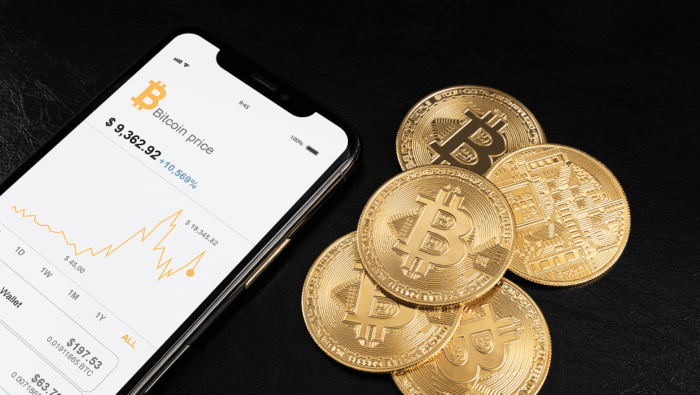 Smartphone showing a Bitcoin price chart beside physical Bitcoin coins