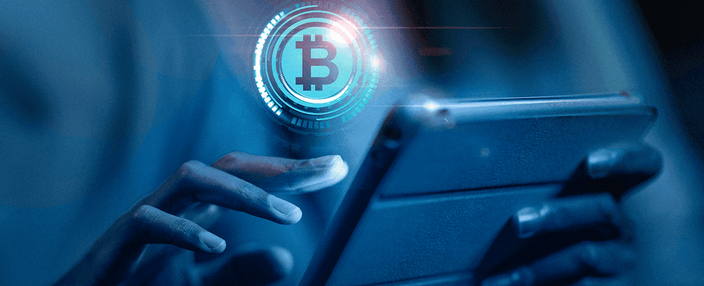 Hands holding a tablet with a glowing Bitcoin hologram