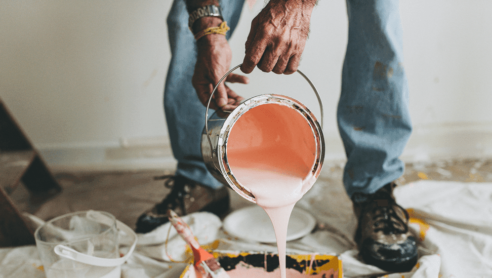 Person pouring pink paint from a metal bucket into a tray